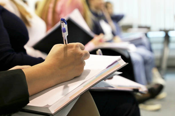 creative writing club images Women sitting in a row in a conference room, female hand with pen writing in a notepad Concept of lecture, business meeting, college classes, skills development, press people, staff training writing workshop stock pictures, royalty-free photos & images
