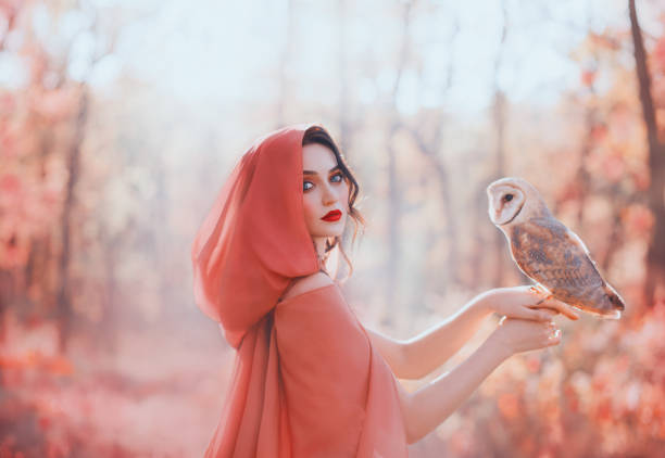 femme païenne mystique avec la tête couverte dans l'écharpe de pêche dans la forêt, tient le petit hibou mignon de grange. dame avec les cheveux bouclés foncés, le maquillage lumineux et la peau pâle juste, fille de la for�êt d'automne s'occupant d - fairy forest women magic photos et images de collection