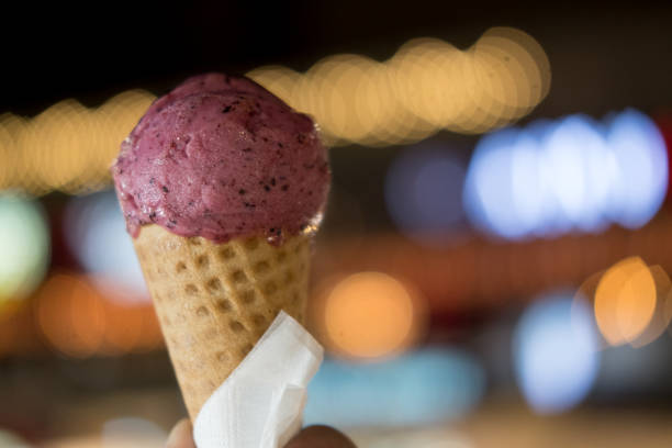 istock Blueberry ice cream in waffle cone on young man hand with light night background 1166628123