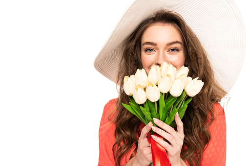 happy elegant woman in hat and dress holding tulips bouquet isolated on white