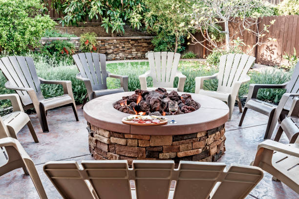 Backyard and Patio Party Setup Large outdoor fire pit surrounded by wooden rocking chairs, beautifully landscaped backyard, with the glass of wine and food platter. round wooden chair stock pictures, royalty-free photos & images