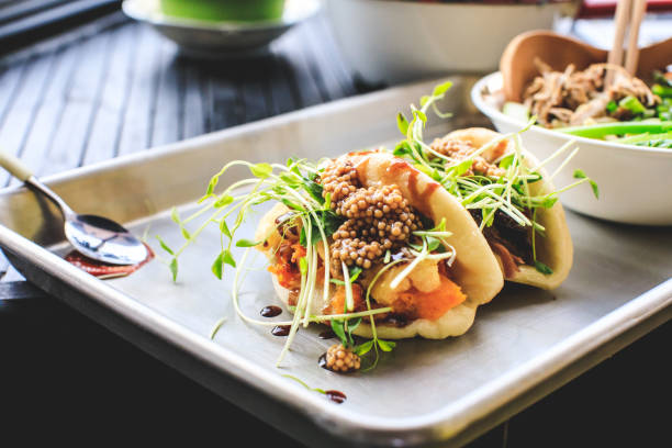 Vegan Steamed Bao Buns And Ramen Two vegan steamed bao buns and a bowl of ramen on a baking sheet tray in a local izakaya fusion food stock pictures, royalty-free photos & images