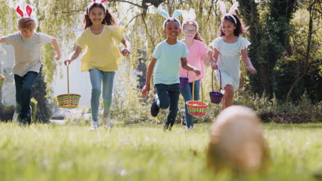 Group of children on Easter egg hunt running across garden and picking up chocolate egg to put into basket - shot in slow motion