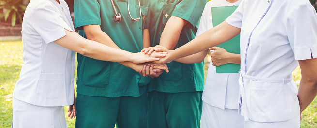 Cooperation of people in the medical community with a hands together between the doctor in the green suit and nurses in white dress to comment provide the most effective treatment to patients at outdoor.