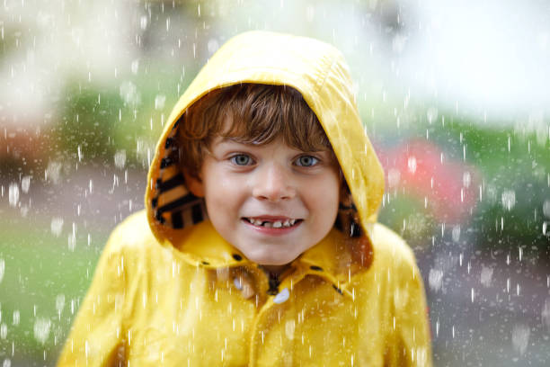 bellissimo bambino mentre va a scuola camminando durante il nevischio, la pioggia battente e la neve con un ombrello nella giornata fredda. bambino felice e gioioso in colorati abiti casual moda cappotto giallo - garment snow little boys child foto e immagini stock