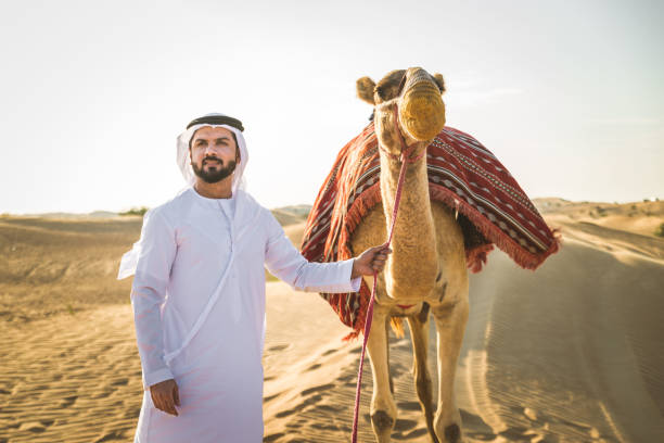 Handsome middle eastern man with kandura and gatra riding on a camel in the desert