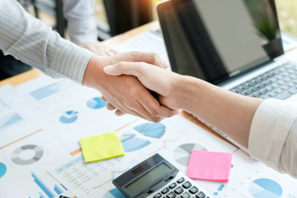 istock Midsection Of Colleagues Handshaking Over Charts On Office Desk 1166643336