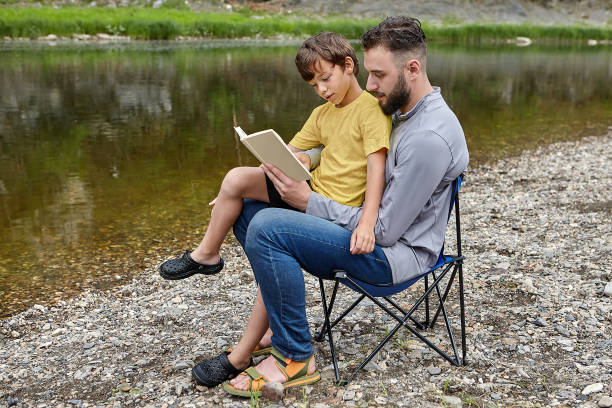 父は自然の中で息子に本を読んでいる。 - uncle ストックフォトと画像