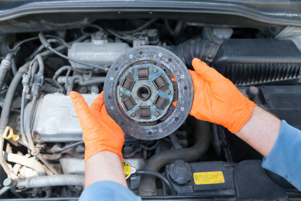 istock Auto mechanic wearing protective work gloves holds old clutch disc over a car engine 1166669648