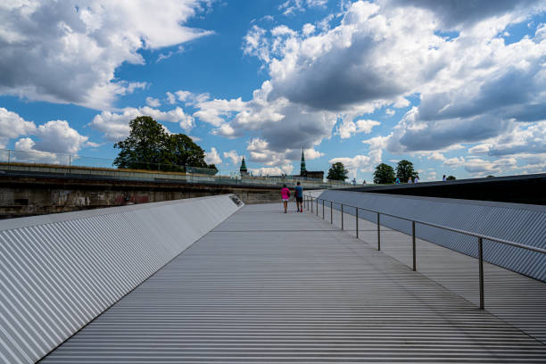 Kronborg, Denmark -- July 26, 2019. Tourists walk along the bridge under a dramatic sky toward the famous Maritime Museum  in Kronborg Denmark; the Kronborg Castle is in the background.