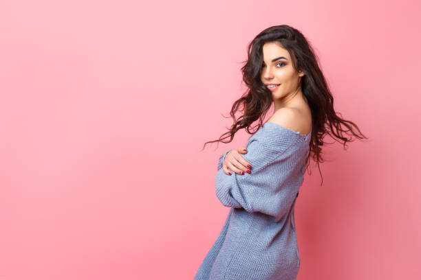 istock Smiling woman dressed in blue knitted sweater looking over shoulder while posing on pink background 1166674386