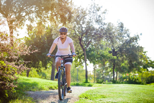 Front view of a mature woman cycling on a mountain bike in an urban park. The woman is wearing sport clothes Predominant color is green. Copy space available for text and/or logo. DSRL outdoors photo taken with Canon EOS 5D Mk II and Canon EF 70-200mm f/2.8L IS II USM Telephoto Zoom Lens