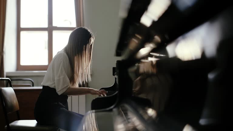 Girl pianist plays classical music on grand piano near the window in slow motion
