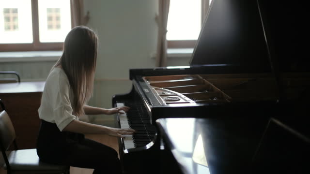 Woman playing the black piano on the background of the window in slow motion
