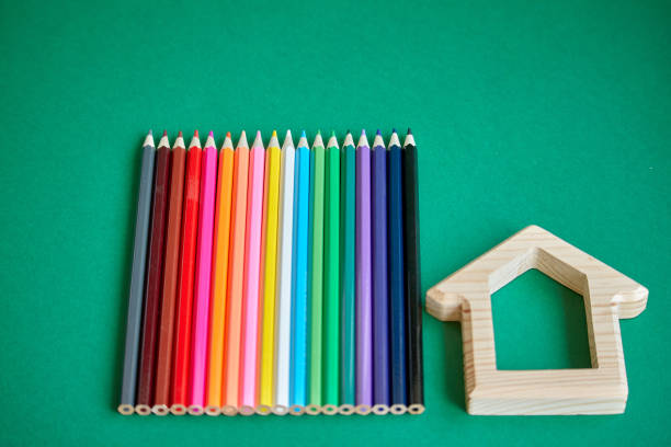 istock Wooden house figurine and several colored pencils isolate on green background, concept back to school, selective focus 1166687164