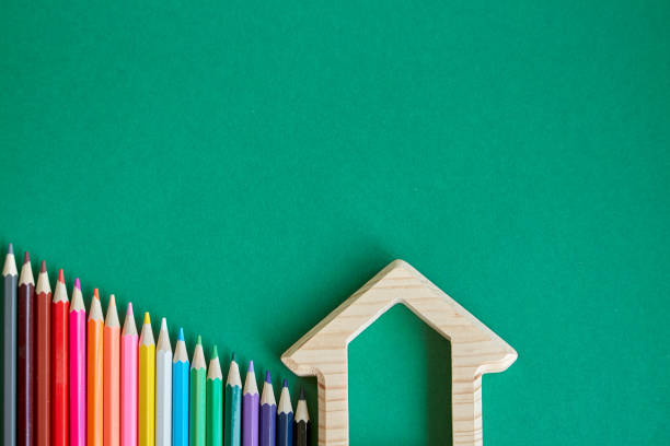 istock Wooden house figurine and several colored pencils isolate on green background, concept back to school, selective focus 1166687165