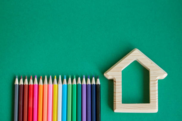 istock Wooden house figurine and several colored pencils isolate on green background, concept back to school, selective focus 1166687177