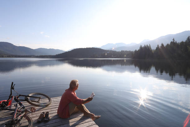 istock Man relaxes on pier beside bicycle, reads book 1166694634