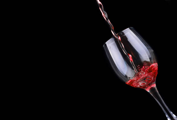 istock Red wine pouring into a wine glass. Isolated on black background 1166703931