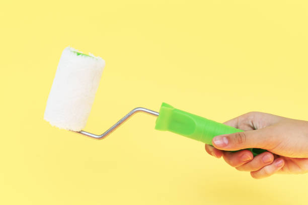 istock Female hand holding paint roller isolated over yellow background 1166704112