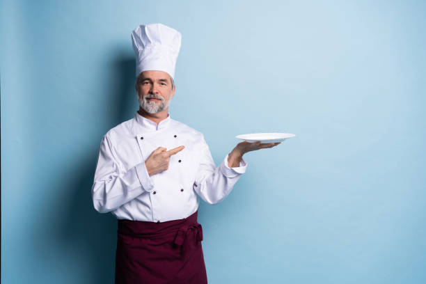 istock Portrait of a professional chef holding an empty plate isolated on light blue. 1166706122