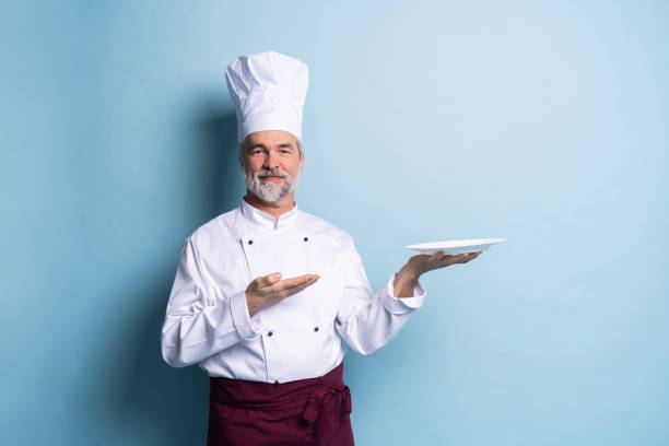istock Portrait of a professional chef holding an empty plate isolated on light blue. 1166706127