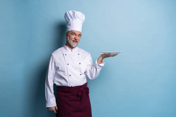 istock Portrait of a professional chef holding an empty plate isolated on light blue. 1166706268