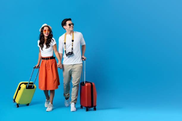 Young couple going for holidays with colorful suitcases Happy young couple being ready to go for their holidays with colorful suitcases isolated on blue background with copy space asian tourist stock pictures, royalty-free photos & images