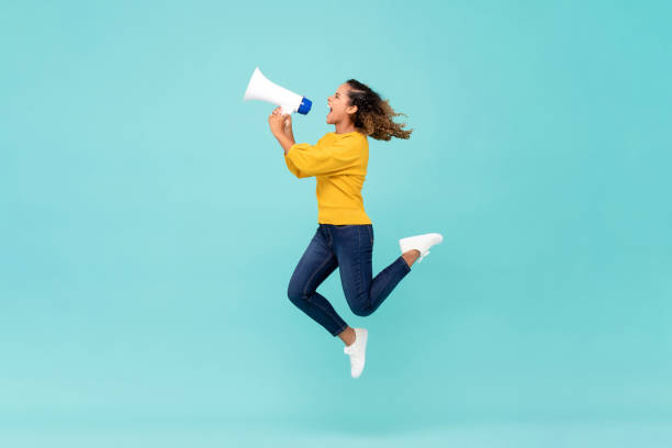 girl with megaphone jumping and shouting - comunicação imagens e fotografias de stock