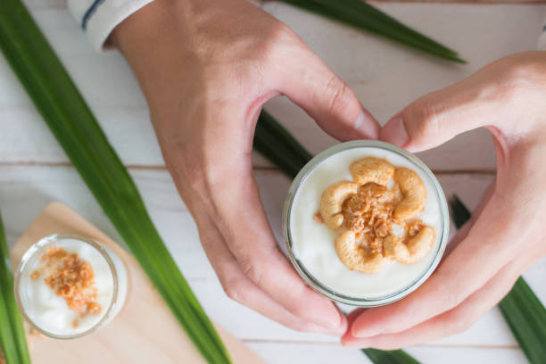 mains retenant le repas sain fait de granola dans le verre, le yaourt et les cornflakes décorent la nourriture avec la noix de cajou à côté a les usines ornementales - tyle photos et images de collection