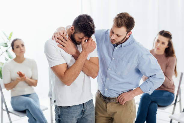 istock man cheering another man while people sitting on chairs during group therapy session 1166725353