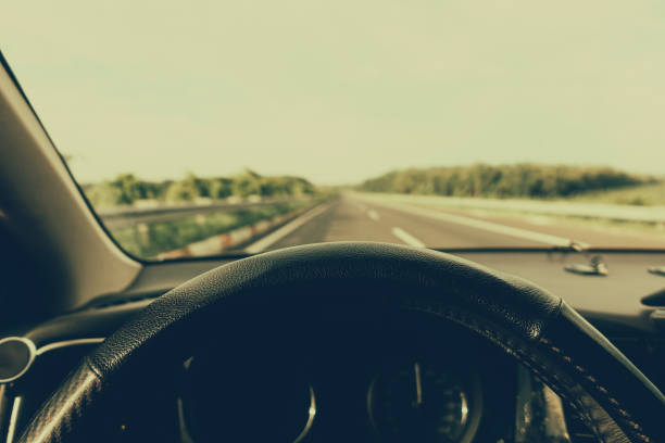 Hands of a driver on steering wheel of a car with empty asphalt road background. High-quality free stock image of driver hands on the steering wheel inside