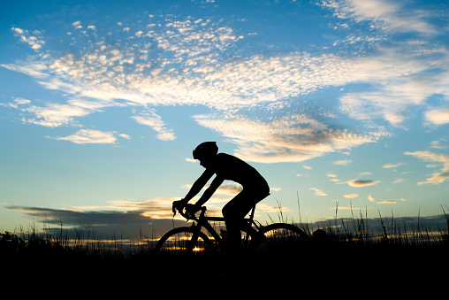 Silhouette of cyclist riding a road bike on open road in evening during sunset. Sports and outdoor activities concept.