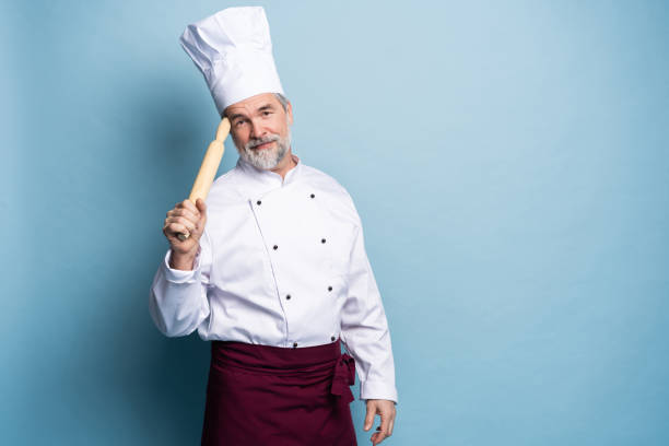 istock Mature professional chef with rolling pin on blue background. 1166727883