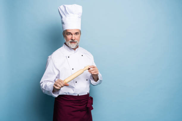 istock Mature professional chef with rolling pin on blue background. 1166727884