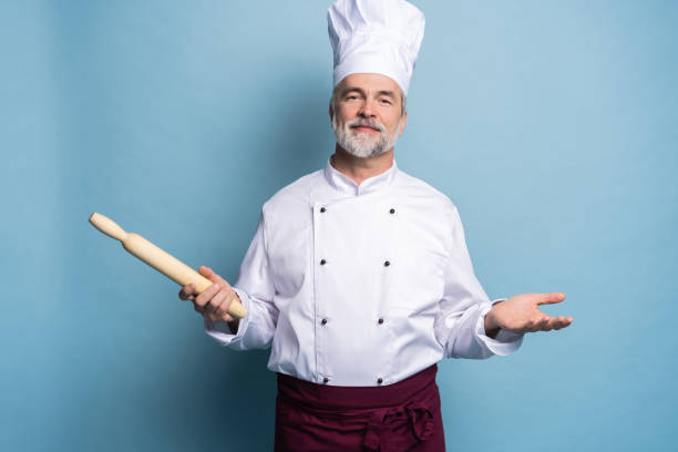 istock Mature professional chef with rolling pin on blue background. 1166727885