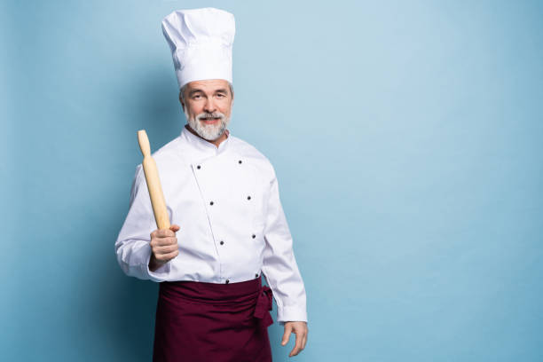 istock Mature professional chef with rolling pin on blue background. 1166727891
