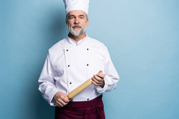 istock Mature professional chef with rolling pin on blue background. 1166727914