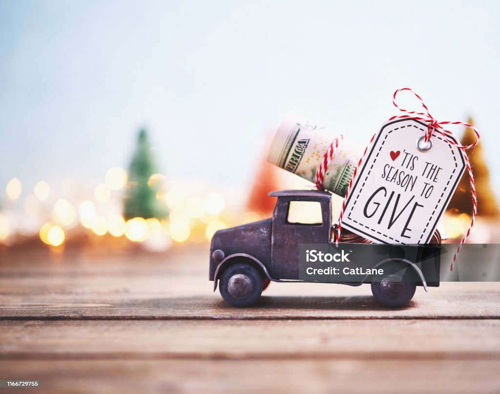 Season to Give. Truck carrying roll of dollars with holiday background Giving Stock Photo