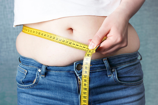 La mano de la mujer mide su estómago con una cinta métrica, concepto de sobrepeso photo