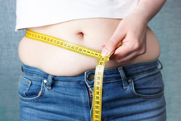 la main de la femme mesure son estomac avec des mesures de bande, concept de surpoids - overweight women abdomen pot belly photos et images de collection