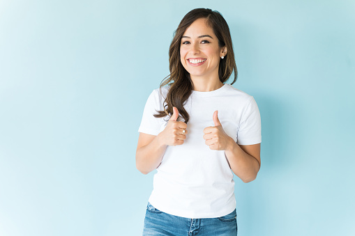 Attractive female showing thumbs up with both hands over blue background