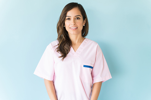 Beautiful mid adult Caucasian nurse wearing scrubs over blue background