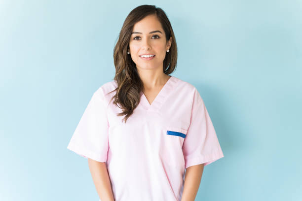Confident Healthcare Worker In Studio Beautiful mid adult Caucasian nurse wearing scrubs over blue background medical scrubs stock pictures, royalty-free photos & images