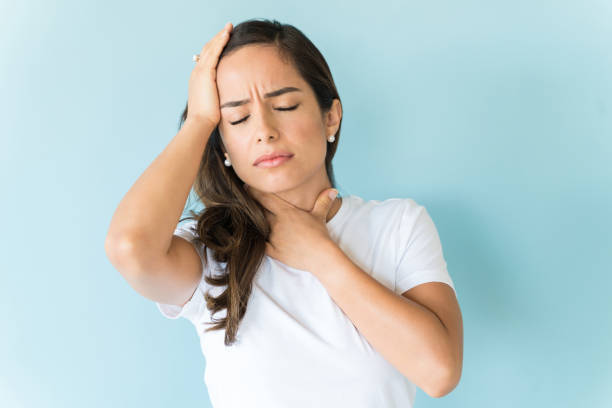Female Grimacing In Pain Over Isolated Background Unhappy ill woman suffering from headache and throat pain against colored background sore throat stock pictures, royalty-free photos & images
