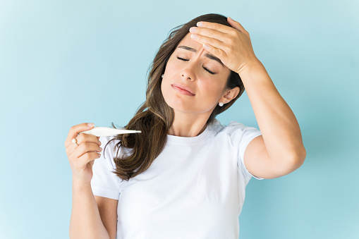 Sick brunette holding thermometer while having headache against blue background