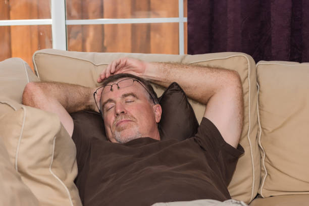 nap with glasses on head A senior man takes an afternoon nap on the sofa or chair enjoying the day in retirement wearing casual clothing. sleeping grandpa stock pictures, royalty-free photos & images
