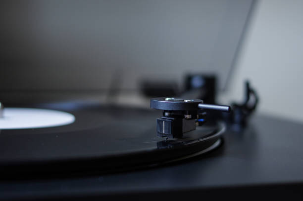 istock Modern round headshell with black cartridge on straight tonearm and vinyl record disc with white label spinning on belt drive turntable 1166757490