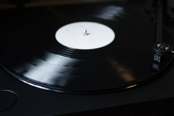 istock Modern round headshell with black cartridge on straight tonearm and vinyl record disc with white label spinning on belt drive turntable 1166757709