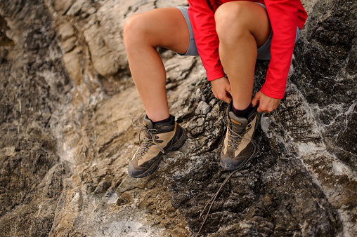 Close-up of female hiker tiyng up shoelaces in hiking boots and sitting on rock